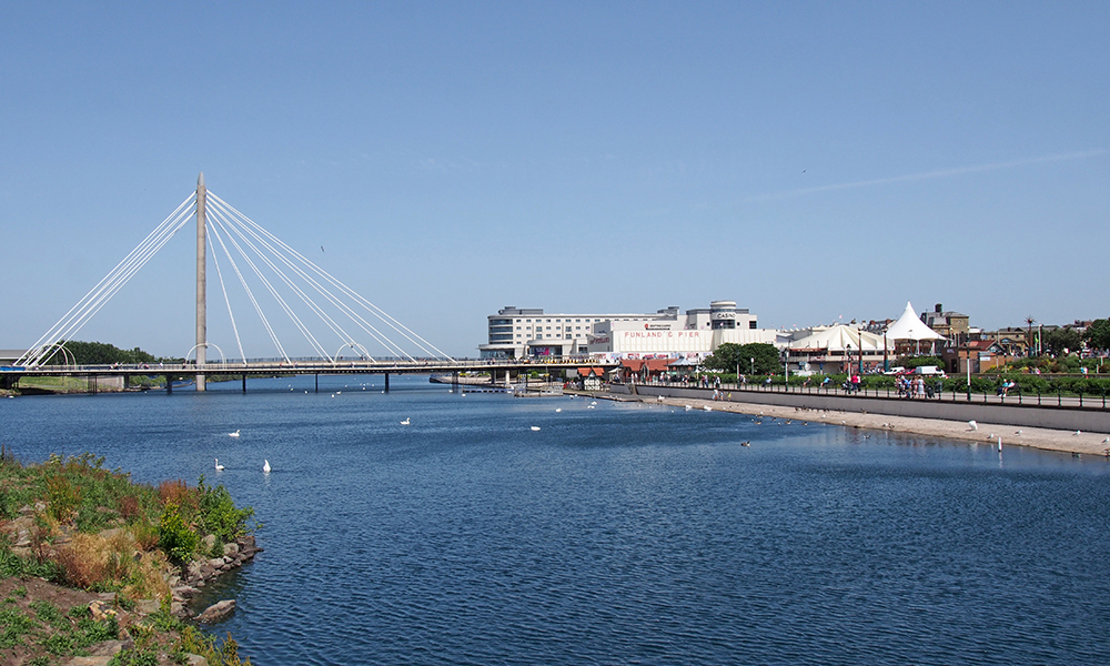 southport, merseyside, united kingdom - 28 june 2019: the suspension bridge and pier crossing the lake in southport merseyside with a view of the town hotels and buildings