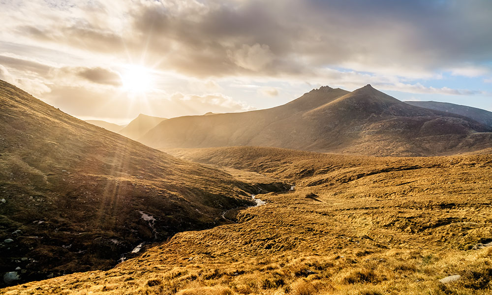 Dramatic sunset with sunrays in beautiful autumn coloured valley with river in Mourne Mountains, highest range in Northern Ireland