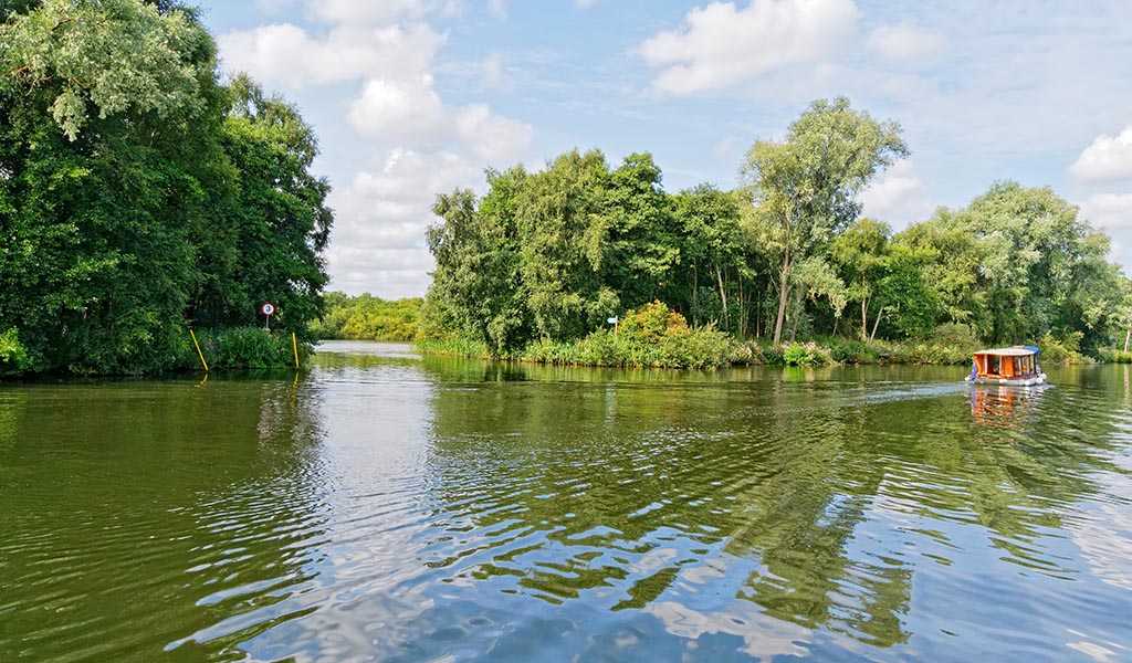 A small cabin cruiser on the River Bure, near Wroxham,passes the entrance to Bridge Broad.