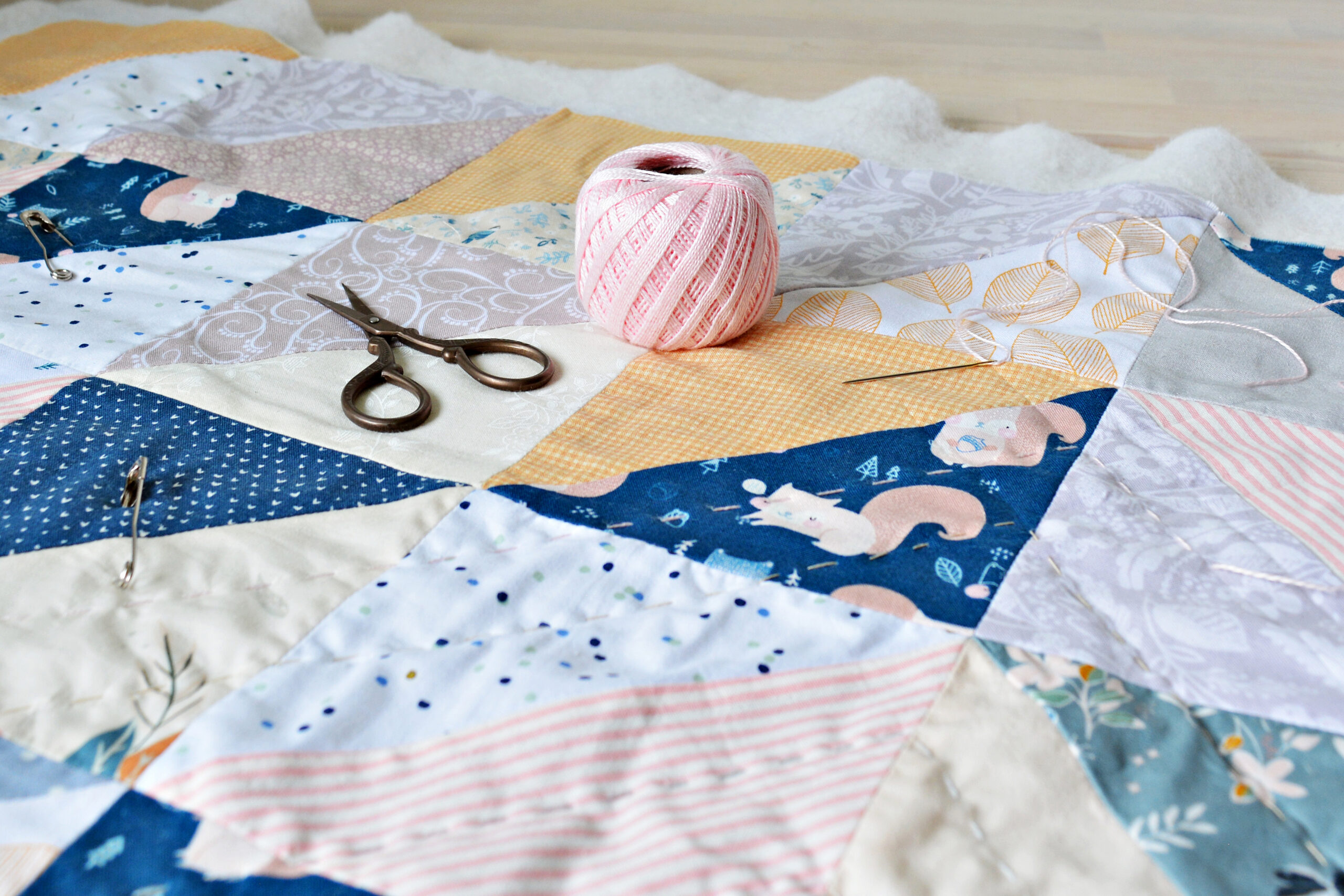 Hand stitch quilting process: cotton thread, needle and scissors on the table