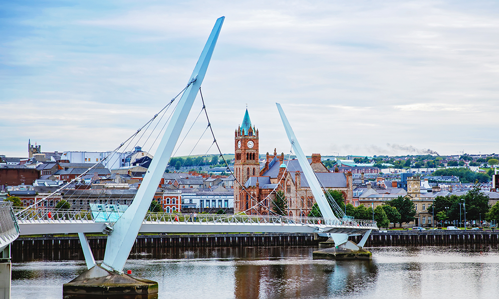 Derry, Ireland. Illuminated Peace bridge in Derry Londonderry, City of Culture, in Northern Ireland with city center at the background. Night cloudy sky with reflection in the river at the dusk.